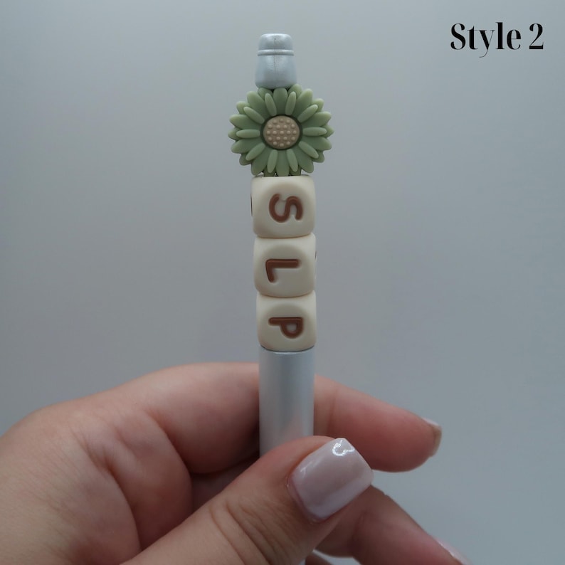 May include: A silver pen with a green flower charm and white letter beads spelling "SLIP".