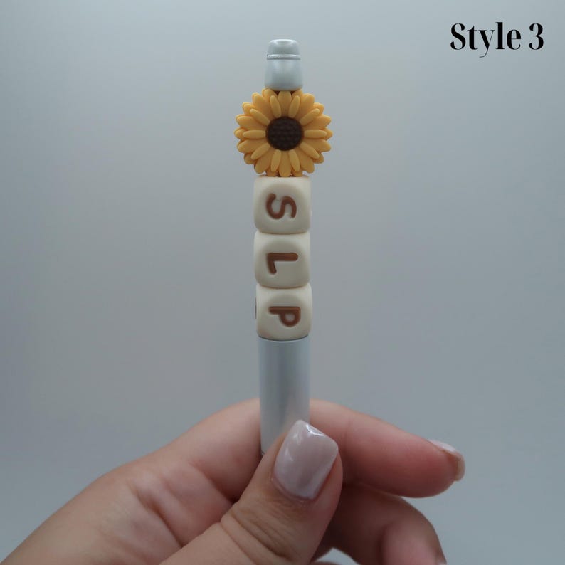 May include: A white pen with a sunflower charm and the word "SLP" spelled out in brown letters on white blocks.