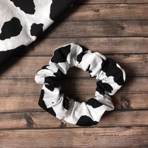May include: A black and white cow print scrunchie hair tie. The scrunchie is made of soft fabric and is perfect for holding hair in place.