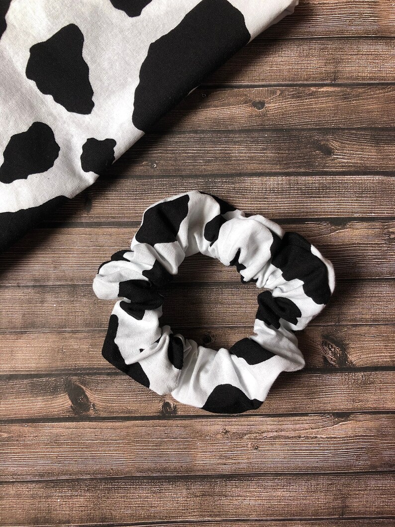 May include: A black and white cow print scrunchie hair tie. The scrunchie is made of soft fabric and is perfect for holding hair in place.