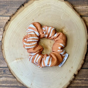 May include: A brown and white striped scrunchie with a white label that says "Small Coast Style".