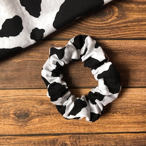 May include: A black and white cow print scrunchie hair tie. The scrunchie is made of soft fabric and is perfect for adding a touch of style to any outfit.