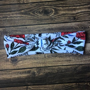 May include: White knotted headband with a floral pattern featuring red roses, green leaves, and the words "Cosmic Warrior".