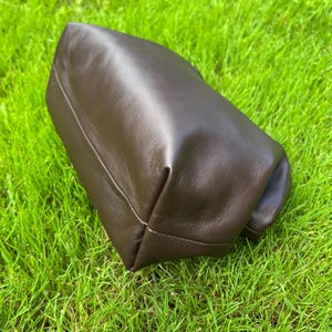 Puede incluir: Un estuche de cuero marr&oacute;n oscuro con un acabado liso y mate y un dise&ntilde;o estructurado y plegado. El art&iacute;culo presenta l&iacute;neas limpias y una textura suave y flexible, mostrando un color profundo y uniforme en toda su superficie exterior.