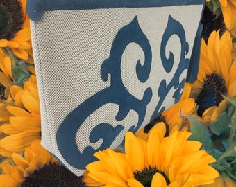 May include: A beige and blue fabric clutch bag with a decorative design. The bag has a zip closure and a tassel.