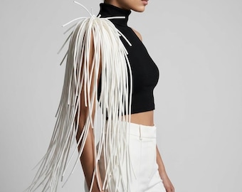 May include: A black sleeveless mock neck top paired with white trousers, featuring a prominent white shoulder accessory composed of numerous long, thin, flexible white tubes that drape downwards like a fringe over the right shoulder.