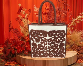 May include: A white tote bag with a brown floral design. The bag has a brown leather handle and is sitting on a wooden platform.
