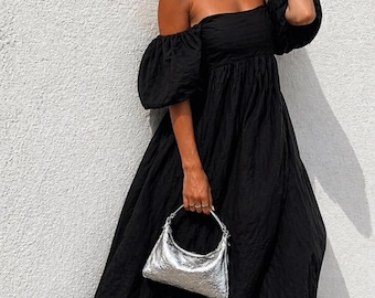 May include: A black off-the-shoulder maxi dress with puffed sleeves and a silver handbag. The dress has a textured fabric and a flowing skirt. The handbag is a small, crescent-shaped bag.