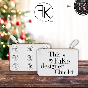 May include: White faux leather clutch bags with gold zippers. One bag has a repeating black logo pattern, the other has the text "This is my FaKe designer Chic'let" in black. The bags are on a wooden surface.