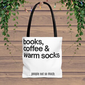 May include: White tote bag with black handles featuring the text "books, coffee & warm socks ...people not so much." The bag is made of a soft material and is perfect for carrying books, groceries, or other items.