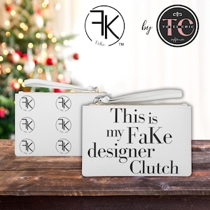 May include: Two white clutches with gold zips and wrist straps. One clutch has multiple black "FK Fake" logos, and the other says "This is my Fake designer Clutch" in black text. The clutches are on a wooden surface.