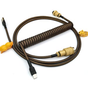 May include: A coiled black and gold USB cable with a gold connector on one end and a USB-C connector on the other end. The cable is decorated with small yellow rubber animal figurines.