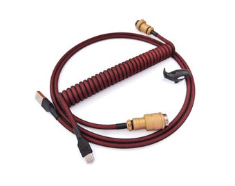 May include: A red and black coiled cable with a gold connector on one end and a USB-C connector on the other end. The cable is coiled in a spiral shape and has a black and red braided sleeve.