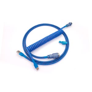 Puede incluir: Cable USB azul en espiral con un conector azul a juego y un pequeño accesorio azul claro. El cable tiene forma de espiral y está sobre un fondo blanco.