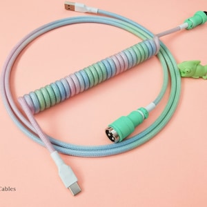 May include: A coiled cable with a pastel blue, green, and pink color scheme. The cable has a USB-C connector on one end and a green connector on the other end. The cable is coiled and has a green alligator charm attached to it.