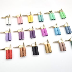Puede incluir: Un surtido de conectores de audio en ángulo de 3,5 mm en varios colores, incluyendo blanco, rosa, amarillo, verde, morado, azul, rojo, marrón, negro y dorado. Cada conector tiene una carcasa metálica dorada.