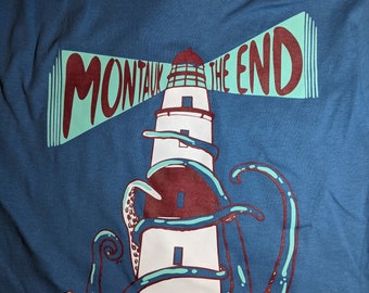 May include: A blue t-shirt with a graphic of a lighthouse being wrapped by an octopus. The text "Montauk The End" is printed on the lighthouse.