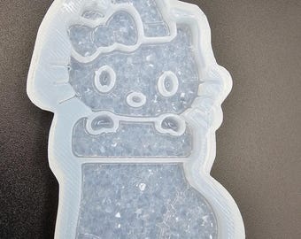 May include: A translucent silicone mold featuring a character with a bow, wearing a hat, and positioned above a stocking shape. The interior of the mold has a textured, glittery surface with a light blue tint throughout the entire form.