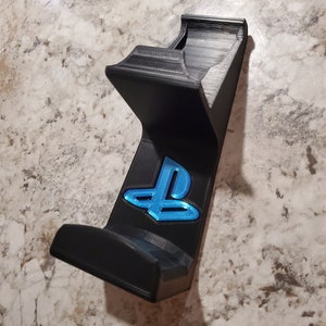 May include: A black 3D printed wall mount for a Playstation controller with a blue Playstation logo.