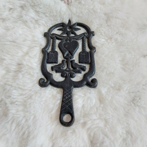 Puede incluir: Un salvamanteles de hierro fundido negro con un diseño de corazón y flores. El salvamanteles tiene un asa y es perfecto para proteger las superficies de los platos calientes.