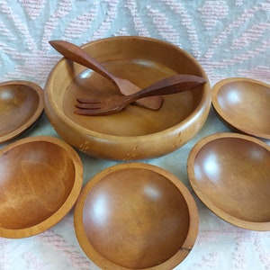 Puede incluir: Un juego de seis cuencos de madera, que incluye un cuenco grande para ensaladas, cuatro cuencos más pequeños y un servidor de ensaladas de madera. Los cuencos están hechos de madera natural y tienen un aspecto cálido y rústico.