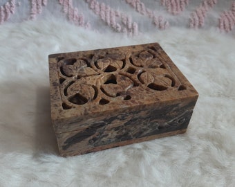 May include: A rectangular brown stone box featuring a carved lid with an intricate openwork leaf pattern. The box displays natural mottled color variations in shades of tan, brown, and dark gray, with a smooth finish on the sides and top surface.