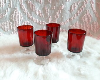 May include: Set of four red glass stemmed shot glasses. The glasses have a clear base and a textured, ruby red body.