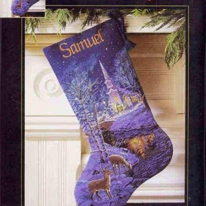 Könnte beinhalten: Ein lila Weihnachtsstrumpf mit einer friedlichen Abendlandschaft, mit einer Kirche, Hirschen und Bäumen. Der Name "Samuel" ist in Gold gestickt. Der Strumpf ist etwa 41 cm lang.