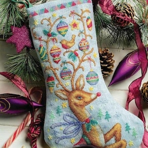 May include: A light blue Christmas stocking with a cross-stitched reindeer design, adorned with colorful ornaments and a bird. The stocking is decorated with a blue bow and green trees. The background includes pine needles, ornaments, and candy canes.