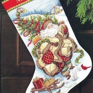 May include: A white Christmas stocking with a red and gold band at the top. The stocking features a winter scene with Santa Claus carrying a bag of gifts and a Christmas tree. The stocking is personalized with the name "Nicholas".