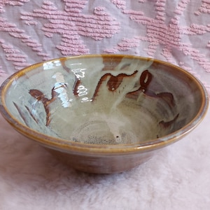 May include: A ceramic bowl with a brown and white glaze. The bowl has a rounded shape and a wide rim.