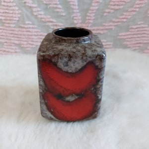 May include: A square ceramic vase with a brown and white speckled glaze and a red glaze design. The vase has a wide opening at the top.