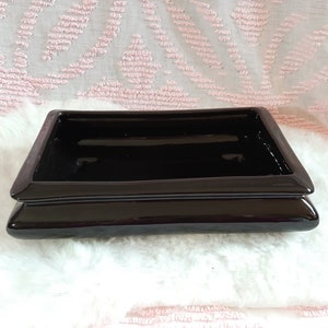 Peut inclure: Un plat rectangulaire en céramique noire brillante avec une base surélevée et étagée. Le plat a une surface lisse et réfléchissante et un design simple et moderne. La couleur foncée et les lignes épurées suggèrent une esthétique minimaliste.