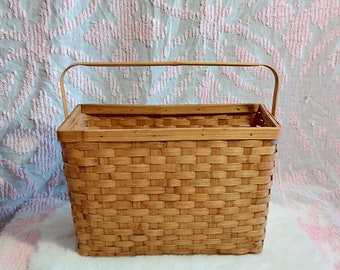 May include: A woven brown wicker basket with a wooden handle. The basket is sitting on a white fluffy surface.