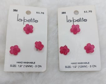May include: Two sets of pink flower-shaped earrings on white cards. Each card has the text "la-petite" and "HAND WASHABLE SIZE: 1/2" (12MM) - 3 ON". The earrings are a vibrant pink color.