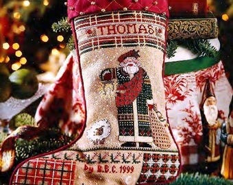 May include: A red and white Christmas stocking with a quilted top and a cross-stitch design featuring Santa Claus, a sheep, and a house. The stocking is personalized with the name "Thomas" and the date "Dec. B.C. 1999".