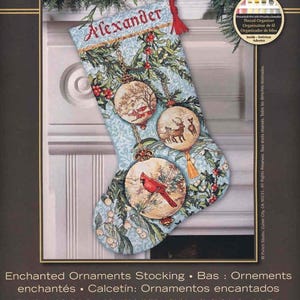 May include: A counted cross stitch Christmas stocking kit titled The Gold Collection Enchanted Ornaments Stocking. The light blue fabric features a pattern of holly, berries, and three circular ornaments depicting a winter scene, deer, and a cardinal.