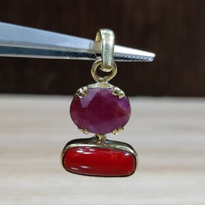 Op de afbeelding: Een gouden hanger met een rode edelsteen en een stuk rood koraal.
