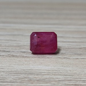May include: A deep red gemstone with a square emerald cut.