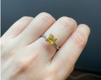 May include: A silver ring with a yellow gemstone. The ring has a twisted band.