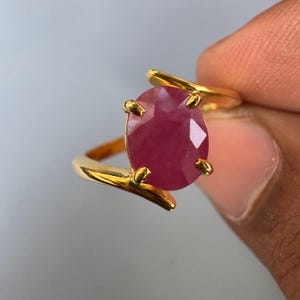 Op de afbeelding: Een gouden ring met een grote, ovale, roze robijn.
