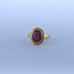 May include: A gold ring with a red oval gemstone set in a rope-like border.