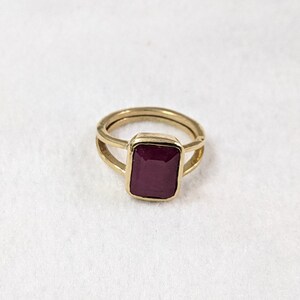 Op de afbeelding: Een gouden ring met een dieprode rechthoekige edelsteen.