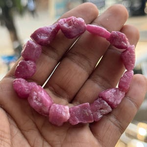 Op de afbeelding: Een armband van roze robijn edelstenen gemaakt van ruwe, ongeslepen stenen. De armband is gemaakt van veel kleine, onregelmatig gevormde stenen.