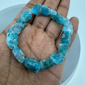 May include: A bracelet made of light blue, faceted, and rough-cut apatite stones. The bracelet is made of natural stones and is approximately 7 inches in length.
