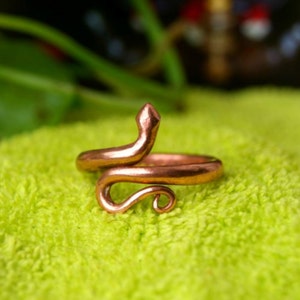 Könnte beinhalten: Ein kupferner Schlangenring mit einem gewundenen Körper und einem erhobenen Kopf. Der Ring liegt auf einem grünen Handtuch.