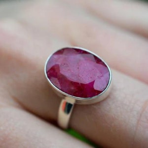 May include: A silver ring with a large, oval-shaped ruby gemstone. The ruby is a deep red color and has a faceted cut.