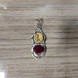 May include: A silver pendant with a red and yellow gemstone setting. The pendant has a bail for attaching to a chain.