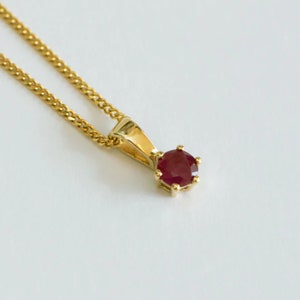 Op de afbeelding: Een gouden ketting met een klein, rond robijn hanger.