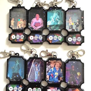 May include: Eight rectangular black resin keychains shaped like concert tickets, each featuring a unique photograph of a performer on stage, silver lobster clasps, and a bottom section filled with colorful confetti and a white logo.